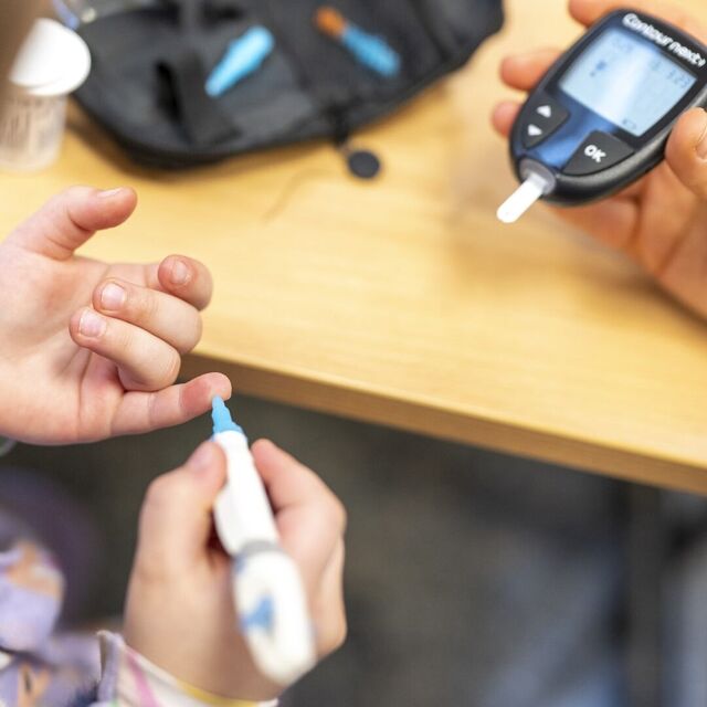 Hände bei einer Blutzuckermessung mit Messgerät und Stechhilfe.