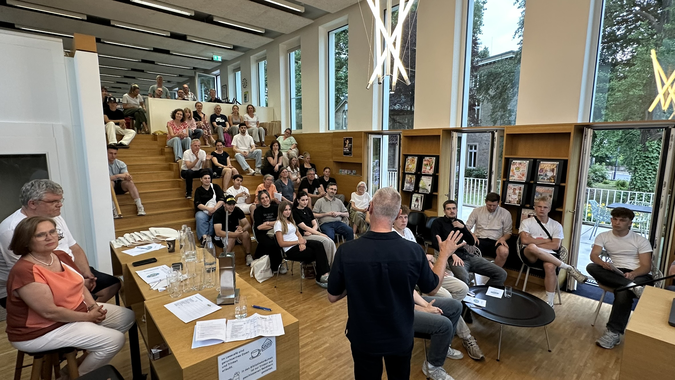 Blick in die Bibliothek Witten beim Science Slam 2026 mit Publikum auf der Sitztreppe und einem Redner im Vordergrund.